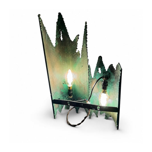 Detalle frontal de lámpara brutalista con siluetas puntiagudas y cordones de soldadura en metal oscuro
