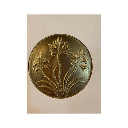 Detalle de placa dorada en relieve con motivos botánicos y firma Ilias LALAoUNIS