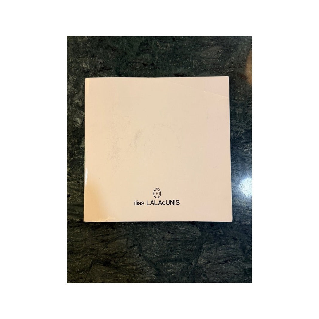 Reverso de tarjeta coleccionable Ilias LALAoUNIS en papel marfil con logotipo de la firma