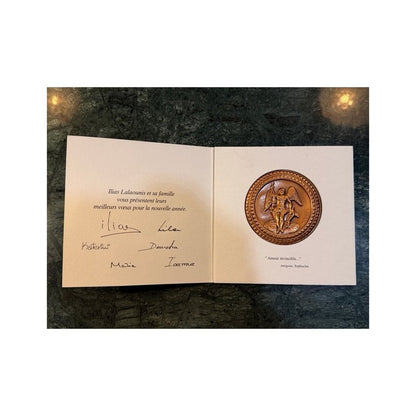 Tarjeta abierta Ilias LALAoUNIS con medallón circular dorado en relieve y figura clásica