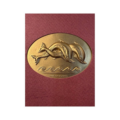 Placa ovalada dorada con dos delfines y ondas marinas en relieve, firmada Ilias LALAoUNIS