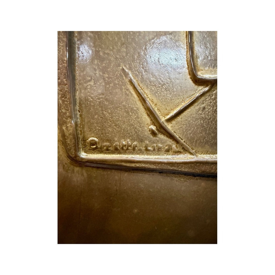 Detalle de la firma en relieve y la textura martillada del panel de metal dorado