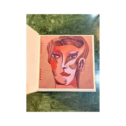 Libro abierto con retrato cubista en tonos coral, rosa y violeta sobre papel artesanal