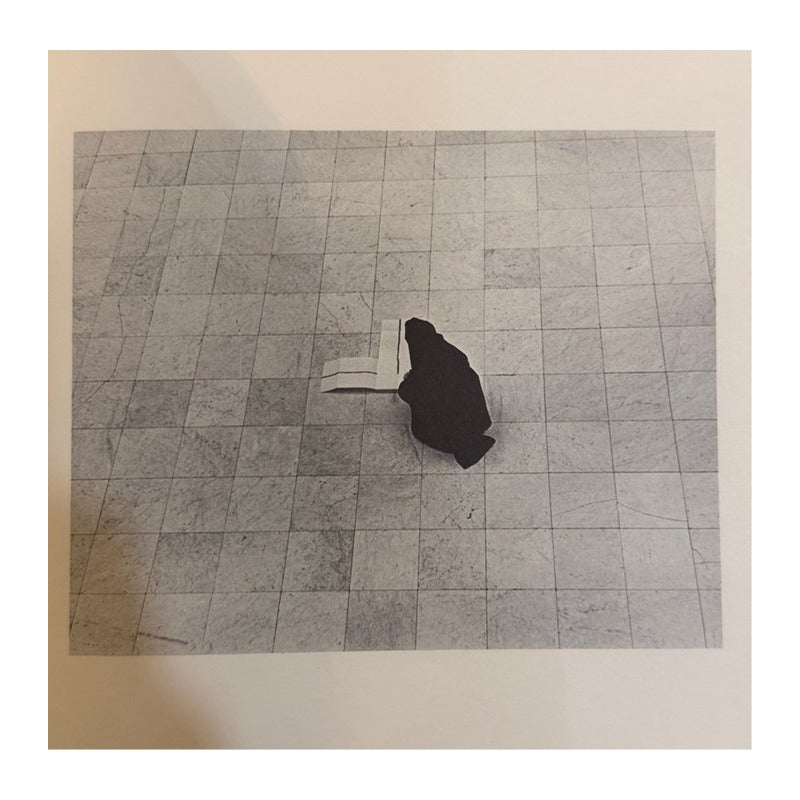 Fotografía en blanco y negro de una figura inclinada junto a un libro abierto sobre suelo de losas