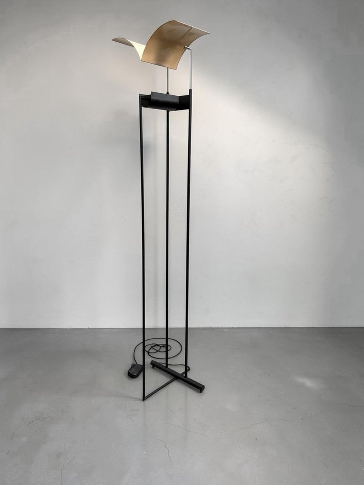 Vista completa de la lámpara Fénix con estructura alta de metal negro y cabezal alado dorado