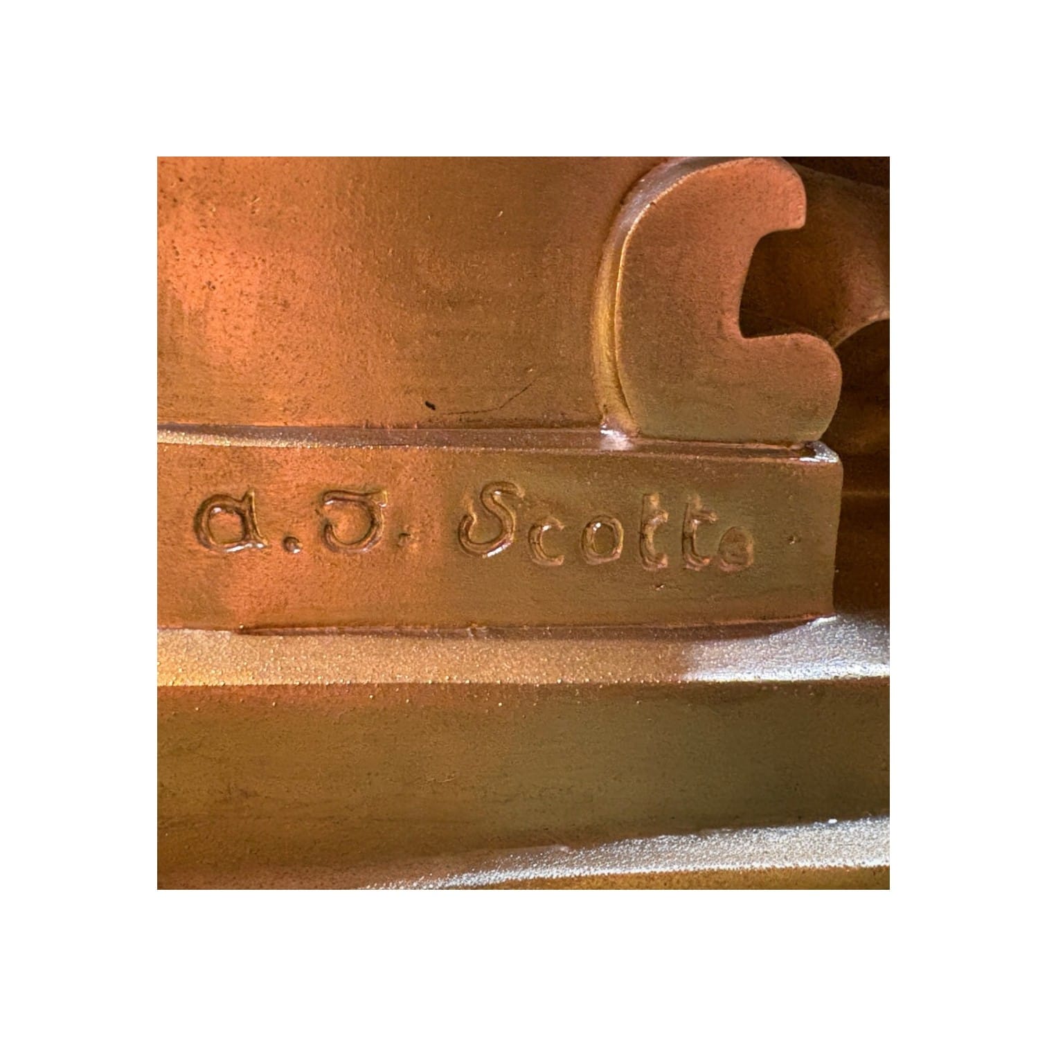 Primer plano del detalle de la firma del escultor "a.J. Scotte" grabada en la base de bronce dorado de la lámpara
