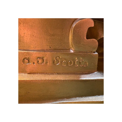 Primer plano del detalle de la firma del escultor "a.J. Scotte" grabada en la base de bronce dorado de la lámpara